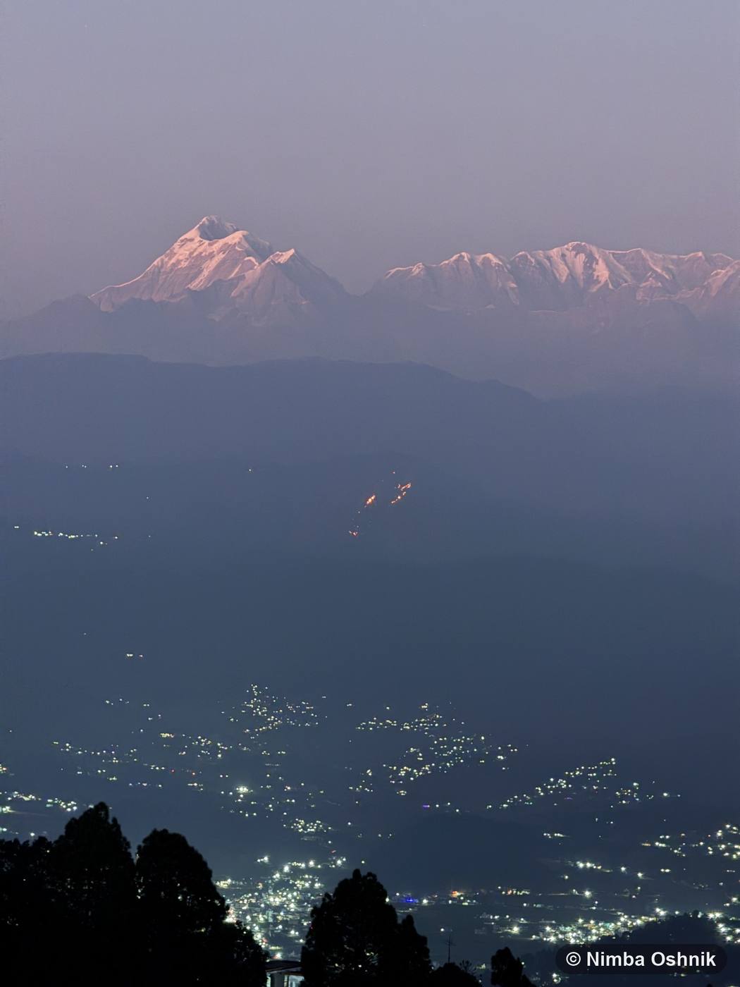 Evening alpenglow on distant snow peaks above a valley town's lights