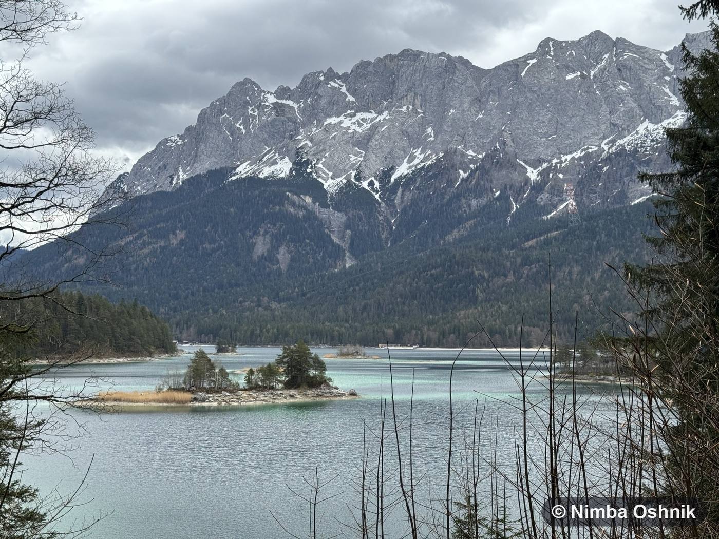 Alpine lake with wooded islets beneath a craggy snow-lined massif