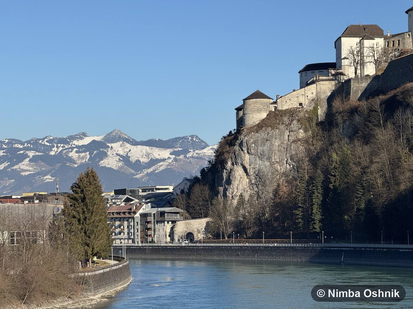 Hilltop fortress towering over a riverside town, snowy peaks behind