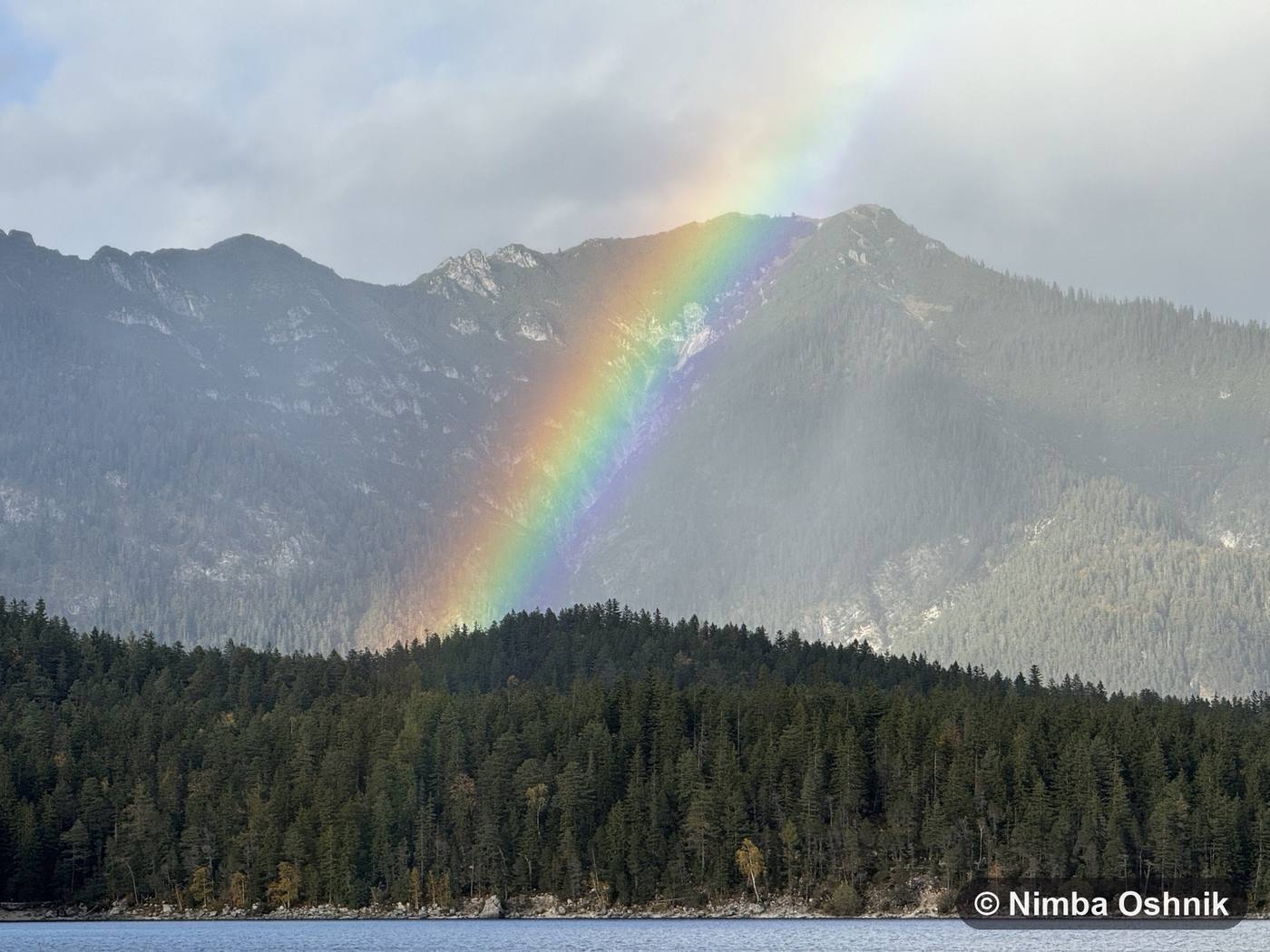 Rainbow arcing over forested mountain slopes