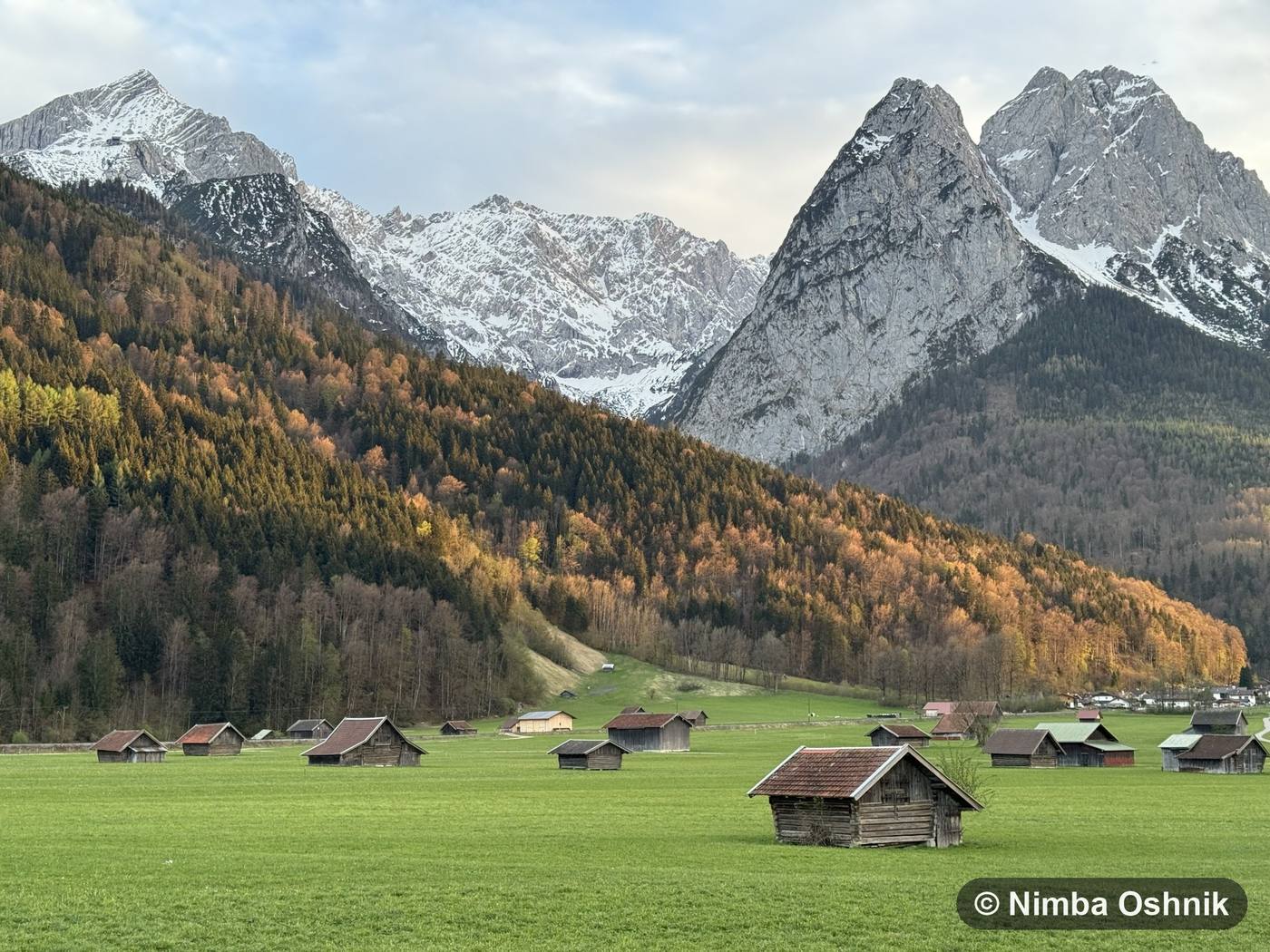 Autumn alpine meadow with hay barns beneath snow-dusted twin peaks